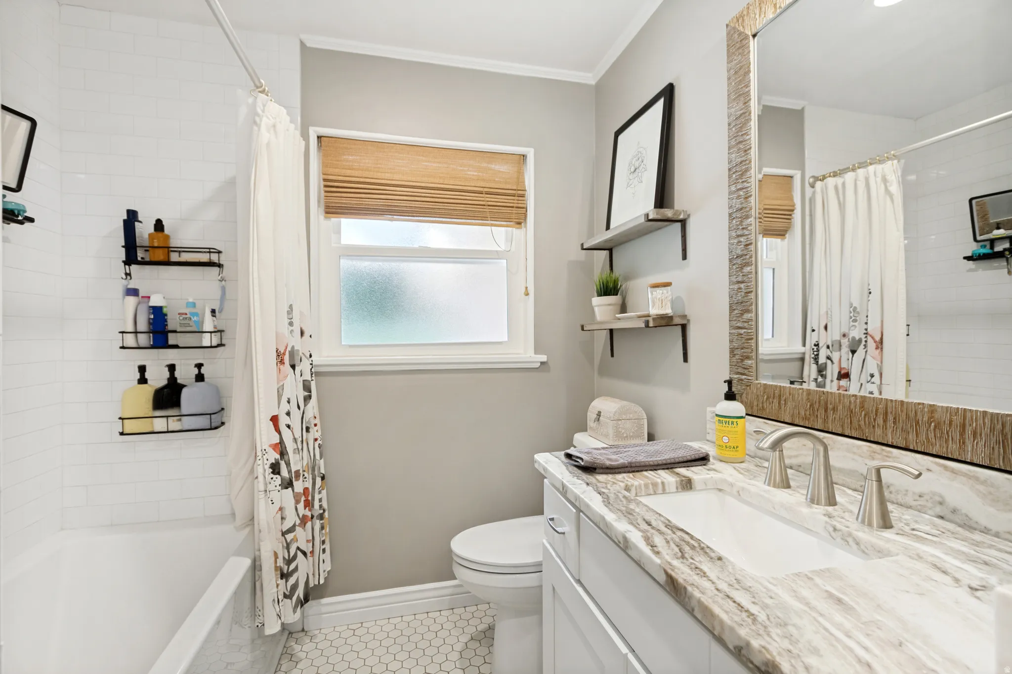 Bathroom featuring a white subway tile shower surround, hexagon tile flooring, a window with a woven wood blind, and a vanity with a stone countertop