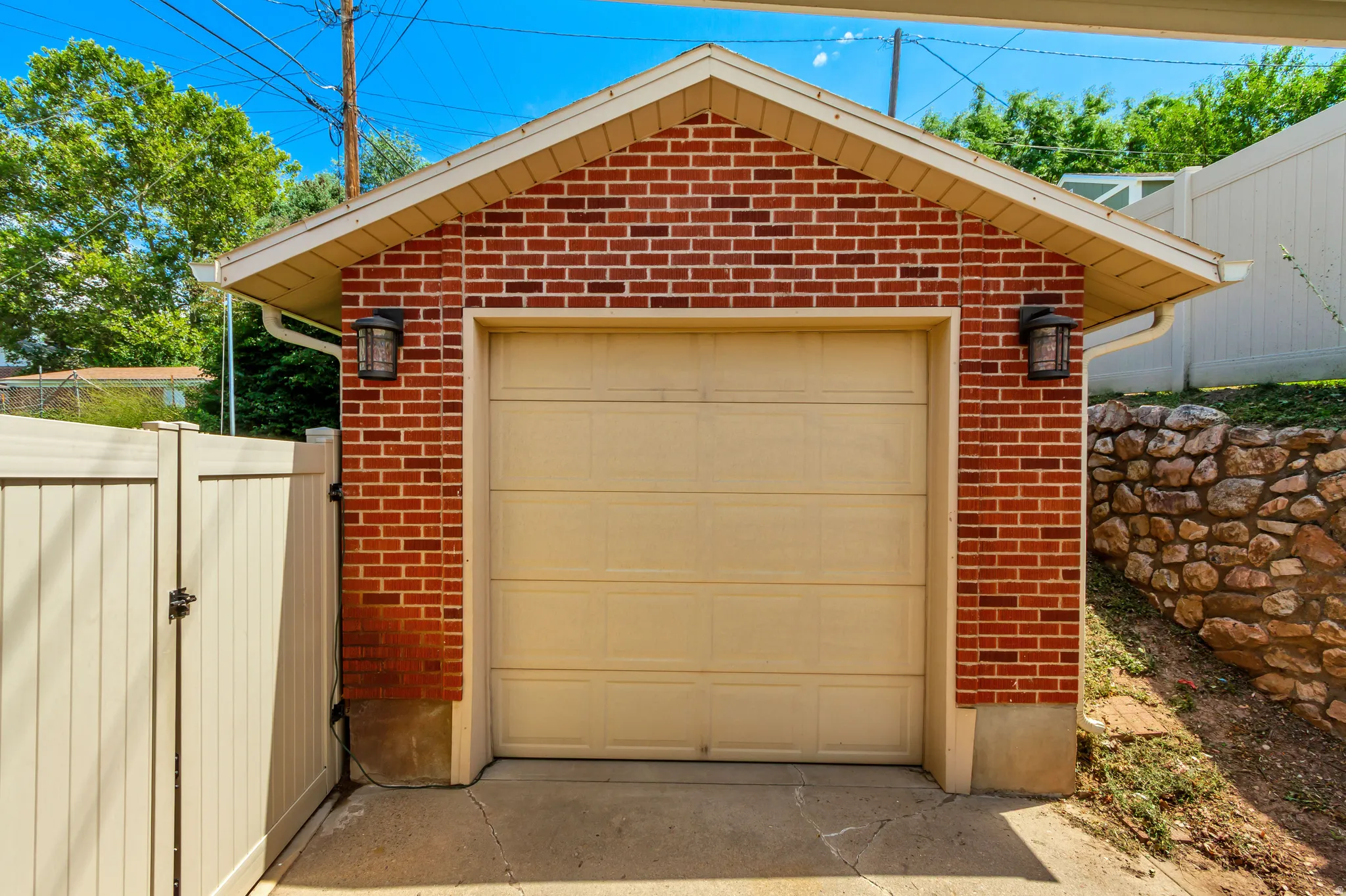 Brick exterior garage with a tan panel garage door, concrete driveway, and built-in exterior lighting fixtures