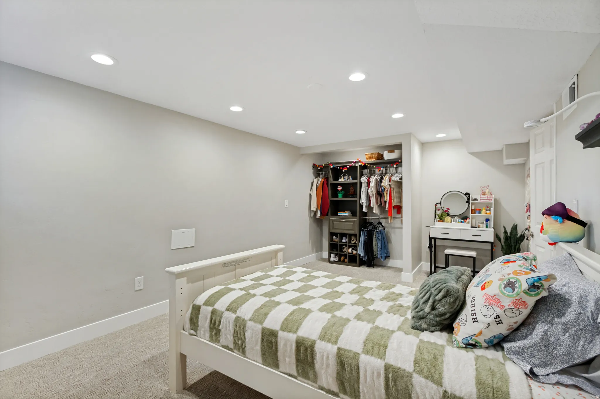 Recessed lighting illuminates a carpeted bedroom featuring neutral paint, white trim, and a built-in closet system