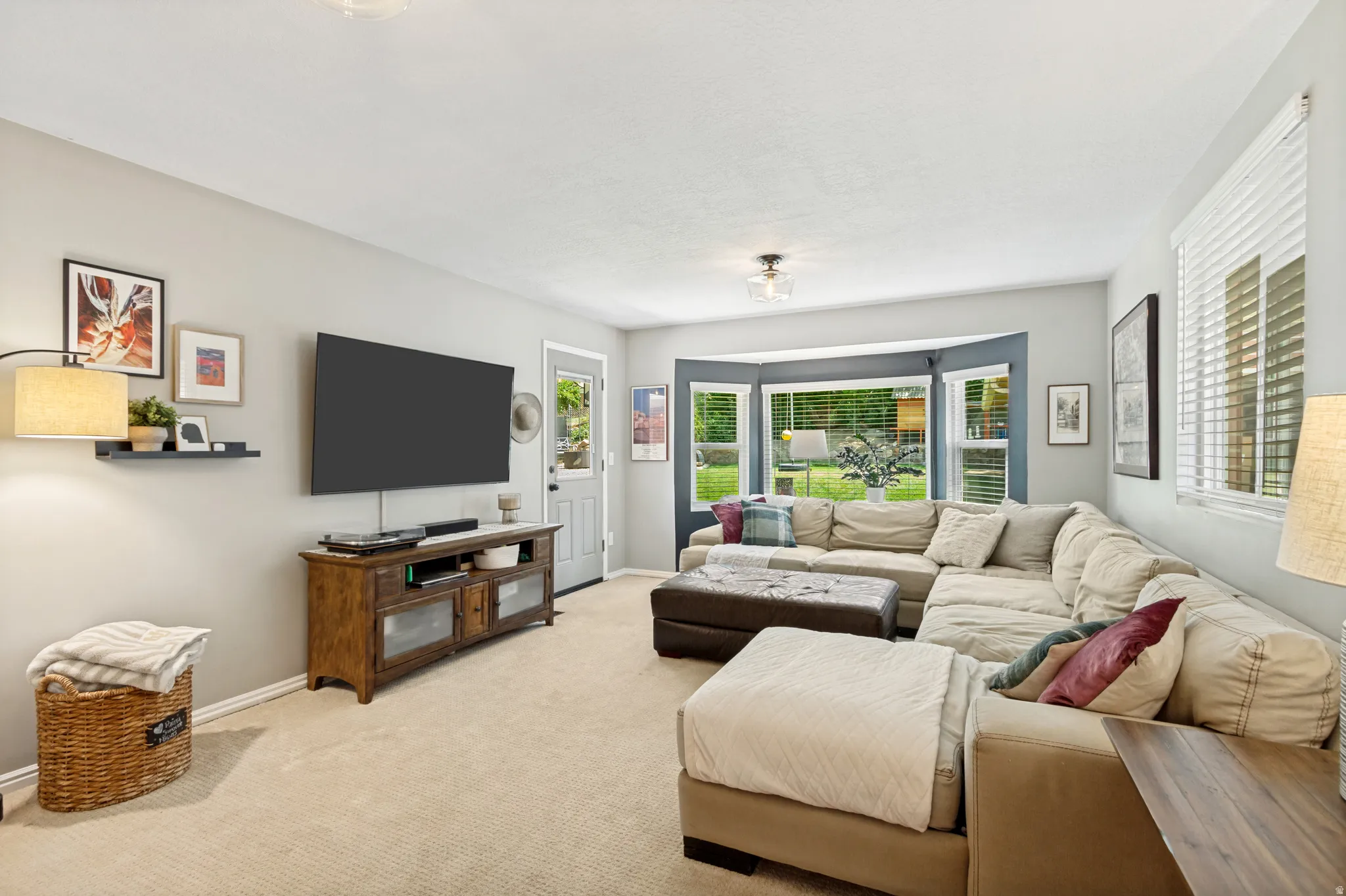Light-filled living area featuring a prominent bay window with exterior views, neutral wall tones, and carpet flooring