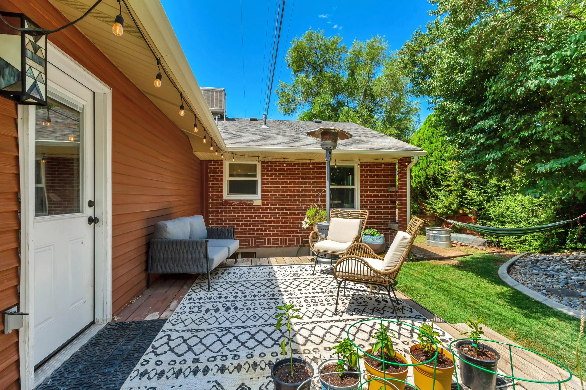 Outdoor wooden deck featuring string lighting, red siding, and a brick exterior building