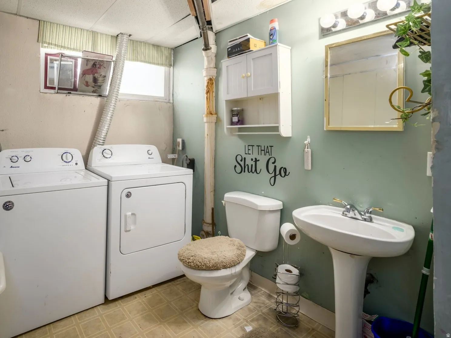 Laundry area with a drop ceiling, pedestal sink, toilet, and exposed piping