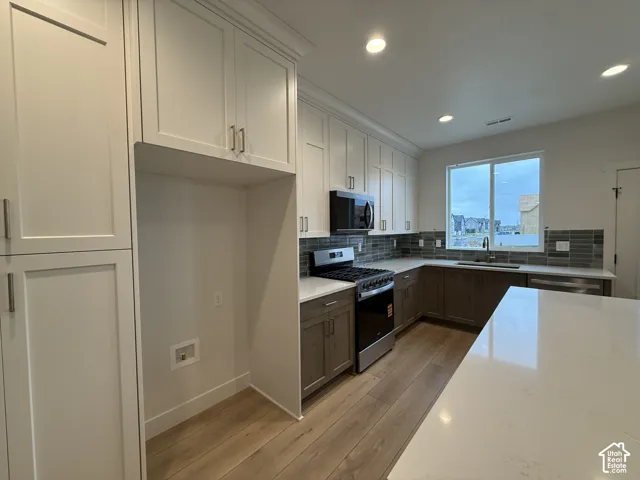 Modern kitchen featuring two-tone cabinetry, stainless steel appliances, a tile backsplash, light-toned wood-finish flooring, and recessed lighting
