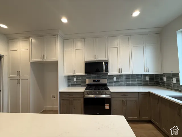 Contemporary kitchen featuring white shaker upper cabinetry, wood-finish lower cabinetry, light-toned countertops, a full stainless steel range, and a subway tile backsplash