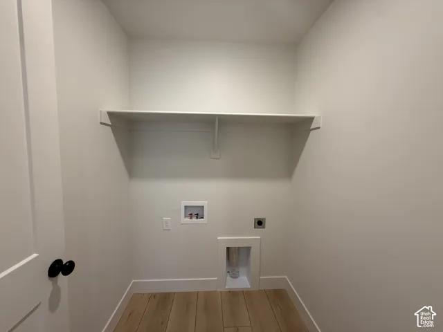 Dedicated laundry area featuring a built-in white shelf, light wood-finish flooring, and white baseboards
