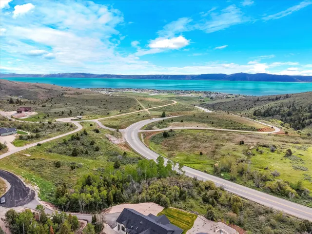 Expansive elevated property featuring a clear turquoise lake, distant mountain range, lush greenery, and paved roadways