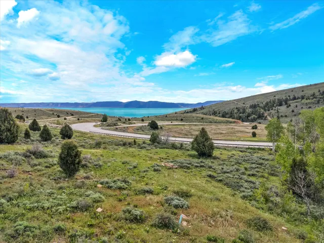 Expansive natural landscape featuring a prominent body of water, rolling hills, and a winding paved road