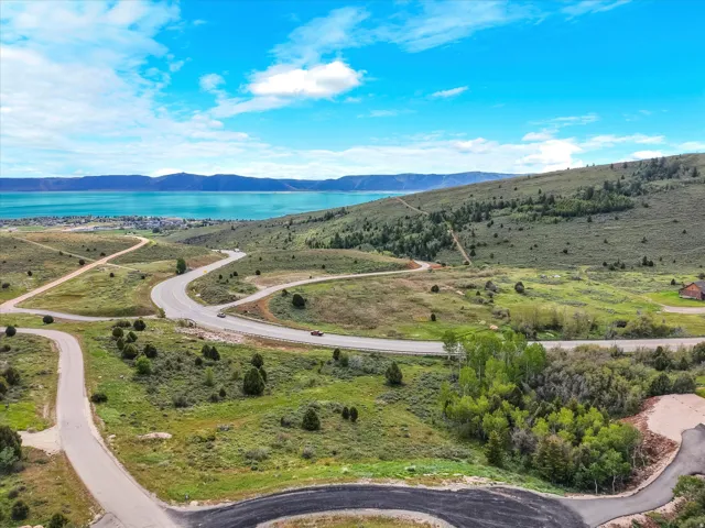 Paved roads traversing rolling green hills with scattered trees, offering distant water and mountain scenery under a bright blue sky