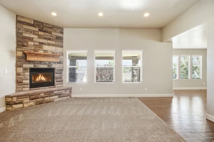Spacious room featuring a corner stone-faced fireplace with a wood mantel, multiple windows with blinds, recessed lighting, and a combination of carpet and wood-finish flooring