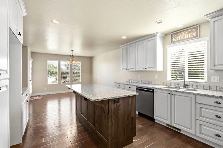 Kitchen featuring a large central island with a granite countertop, white shaker-style cabinetry, wood-finish flooring, stainless steel dishwasher, and a double basin sink