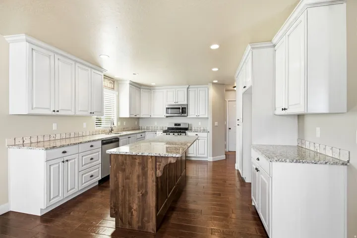 Spacious kitchen featuring white cabinetry, a wood-finish island, granite countertops, and wood-finish flooring