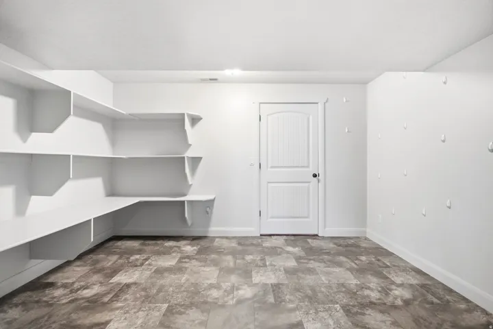 Spacious utility room featuring extensive built-in shelving, durable tile-look flooring, recessed lighting, and a paneled door with dark hardware