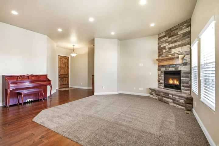 Living area featuring a corner stone fireplace with a wood mantle, recessed lighting, and a combination of wood-finish flooring and neutral carpet