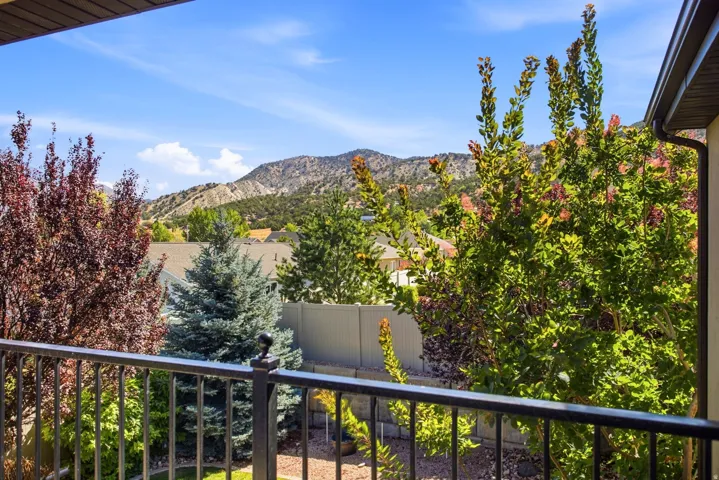 Balcony with black metal railing overlooking a mountain landscape with varied trees and blue sky