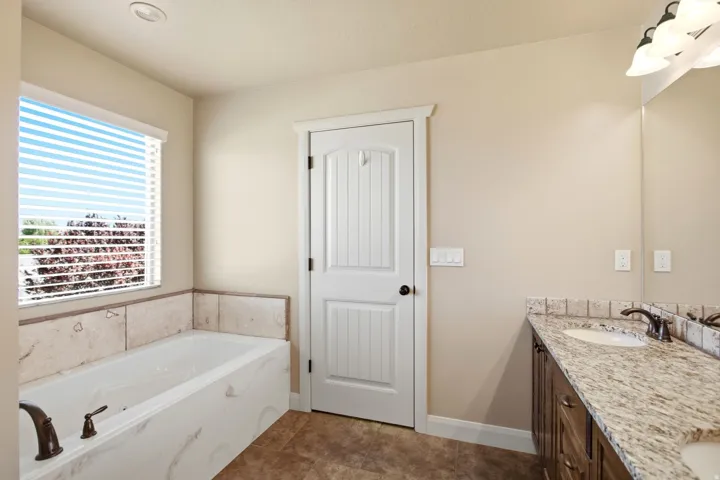 Bathroom featuring a built-in tub with a tiled surround, a window with blinds, and a vanity with a light-toned countertop, integrated sink, and an overhead lighting fixture