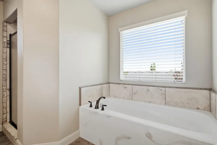 Soaking tub with a tiled surround and a window with blinds