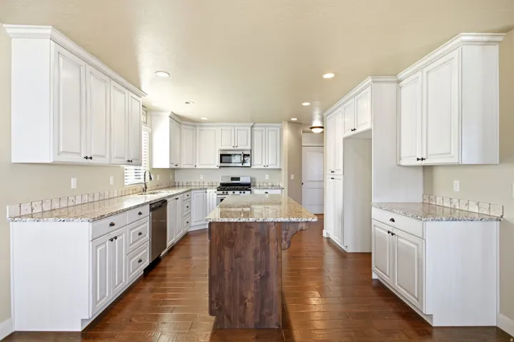 Open-concept kitchen featuring white shaker cabinetry with dark hardware, granite-finish countertops, stainless steel appliances, and a wood-finish island with corbel accents