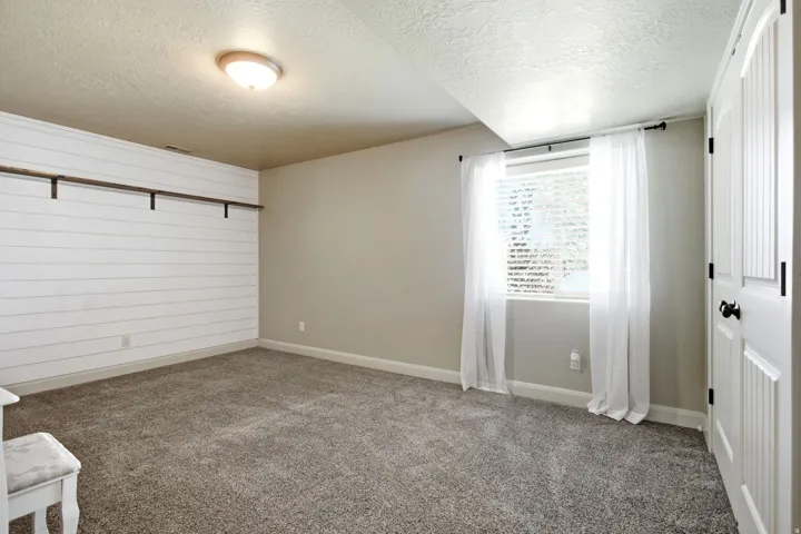 Carpeted room featuring a white shiplap accent wall with built-in shelving, a window with white blinds, and a white panel door with black hardware
