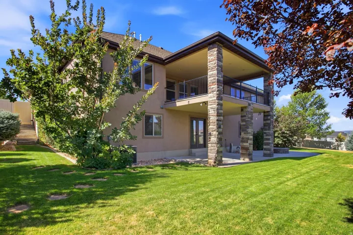 Rear exterior featuring a covered deck, stone columns, ground-level patio, and a terraced backyard