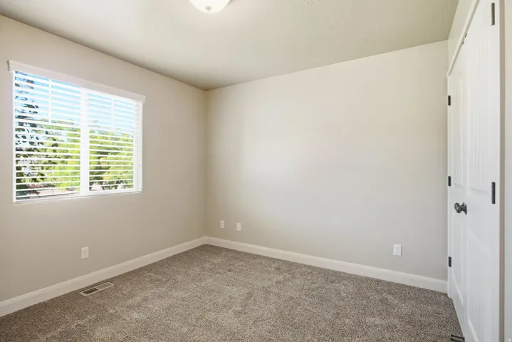 Light-filled interior space featuring neutral wall tones, plush carpet, and a window with horizontal blinds