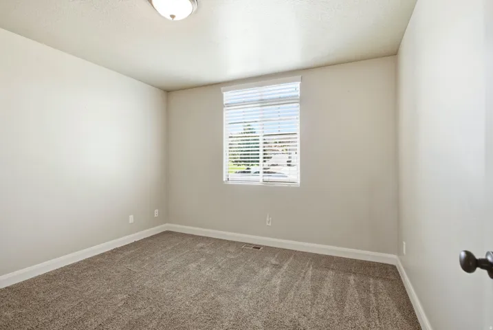 Carpeted interior room featuring a single window with blinds and a flush-mount ceiling light fixture