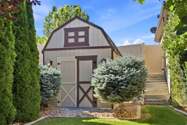 Barn-style shed with a gambrel roof and decorative window, featuring dual doors with cross buck accents