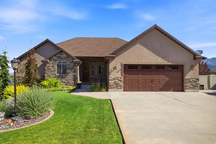 Contemporary exterior featuring a stone and stucco facade, an attached two-car garage, a concrete driveway, a shingled roof, and a mature landscaped front yard