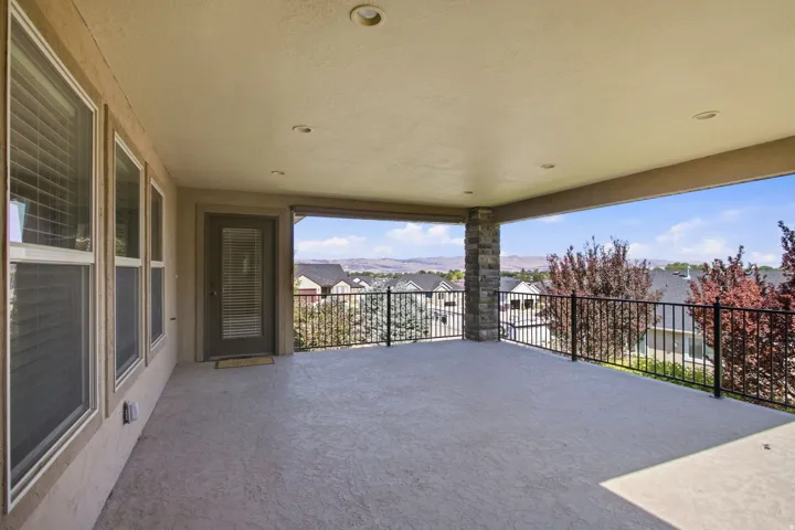 Covered patio featuring a stone-clad pillar, textured concrete flooring, recessed lighting, and a black wrought iron railing