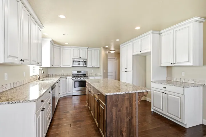 Spacious kitchen featuring white shaker-style cabinetry, granite countertops, a large wood-finish island with granite top, stainless steel appliances, and wood-finish flooring