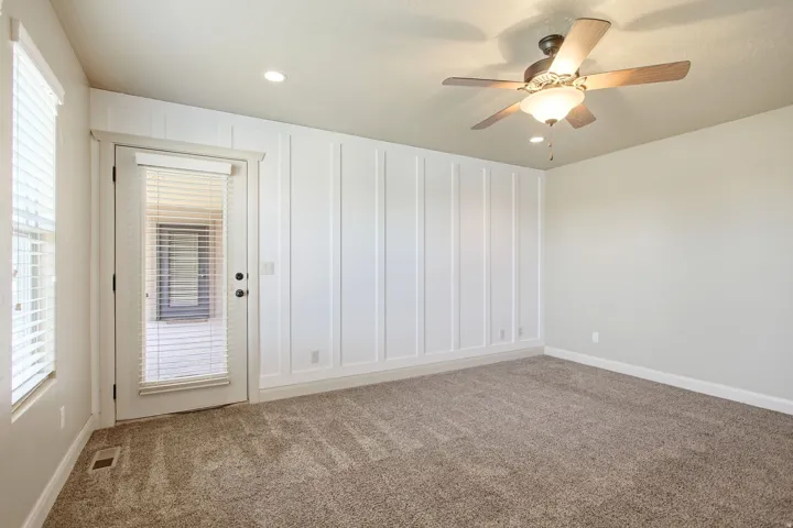 Interior room featuring a white board and batten accent wall, neutral carpeting, and a glass-paneled exterior door with blinds