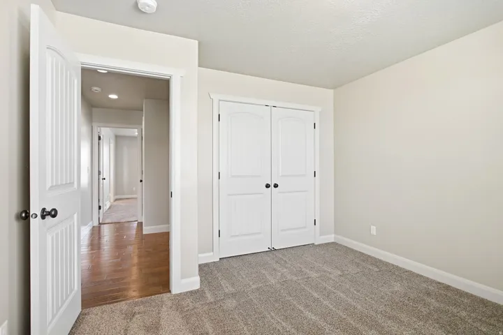 Carpeted room featuring a white bi-fold closet, white baseboards, and a doorway with a full panel door