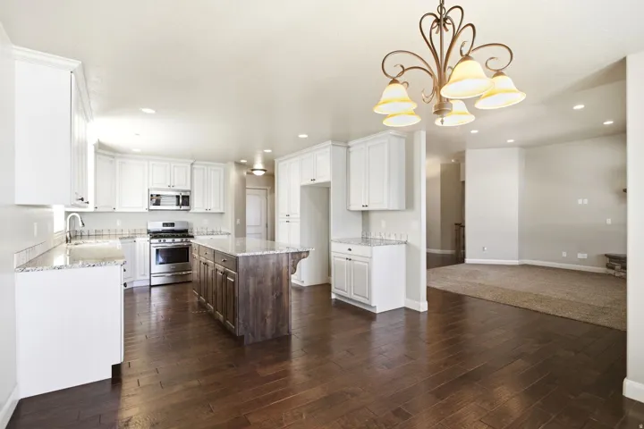 Open-concept kitchen featuring white shaker cabinetry, stainless steel appliances, granite countertops, and a wood-finish island with a contrasting finish