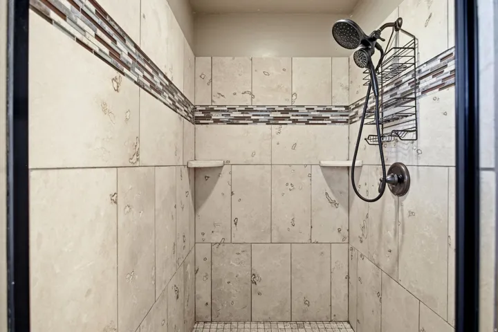 Tiled shower enclosure featuring light-toned large format wall tiles, a mosaic accent band, and a dual-head shower system with an oil-rubbed bronze finish