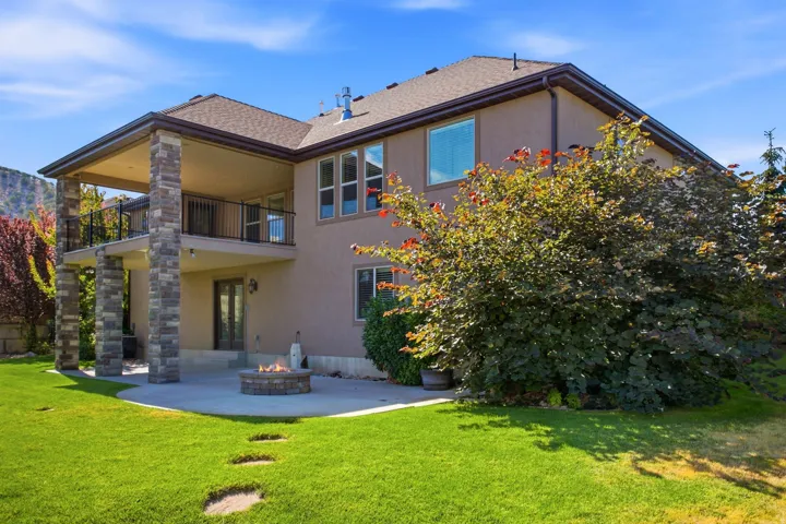 Rear exterior with a stone-clad, covered upper deck and a ground-level patio featuring a built-in fire pit