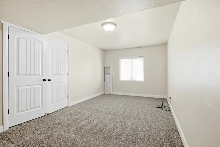 Neutral tone wall finishes, gray textured carpeting, and a single window with white blinds