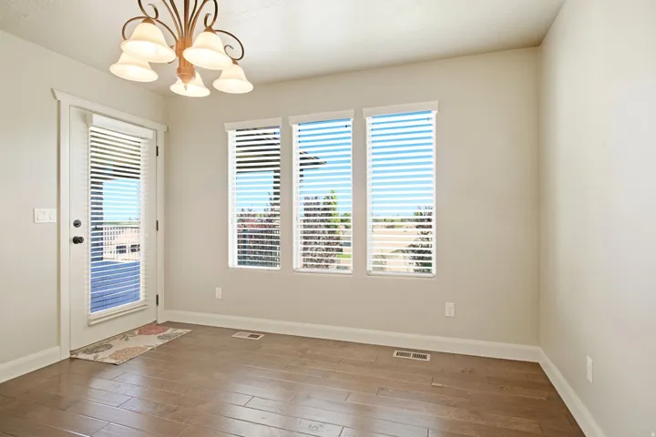 Spacious room featuring wood-finish flooring, a contemporary chandelier, multiple windows with blinds, a glass-paneled door, and neutral wall tones