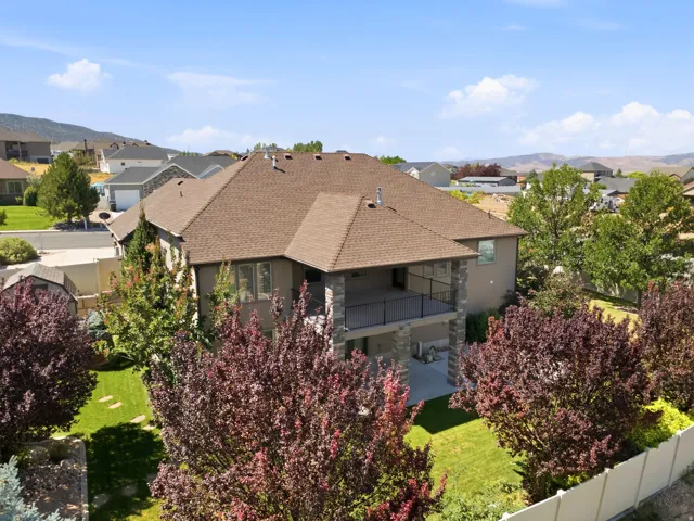 Rear exterior featuring a covered upper-level balcony with black railing, a lower-level patio, and stone column accents