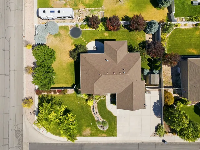 Aerial view showcasing a brown shingled roof, extensive concrete driveway, and a spacious green lawn