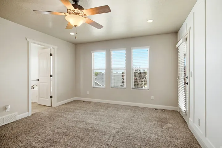 Spacious room with plush carpeting, three windows with horizontal blinds, and a paneled wall featuring a glass-paned door