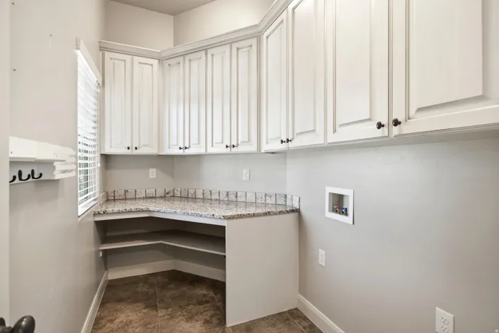 Laundry area featuring extensive white cabinetry, granite-finish countertops, an integrated lower shelf system, and tiled flooring