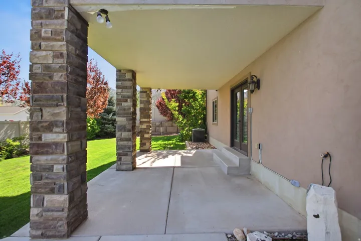 Covered patio featuring stone-clad pillars, concrete flooring, and an outdoor wall sconce