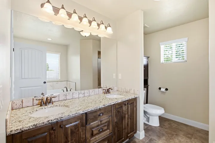 Bathroom featuring a double vanity with granite countertops, wood-finish cabinetry, and undermount sinks