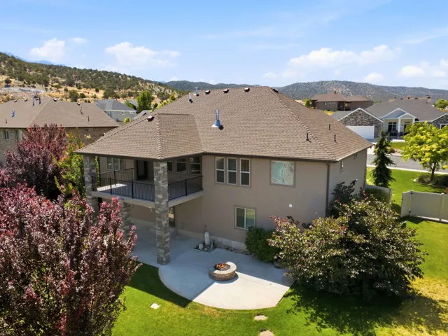 Rear exterior featuring a covered deck supported by stone-clad columns, a ground-level concrete patio, and a built-in fire pit