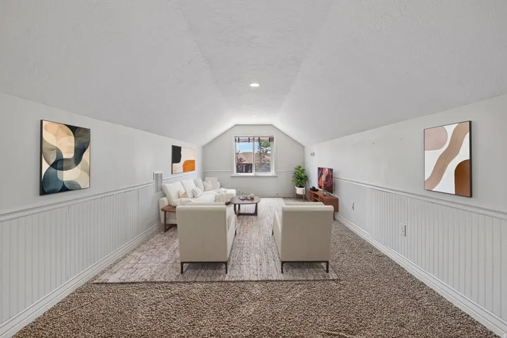 Spacious room featuring vaulted ceilings, a window providing natural light, and wainscoting