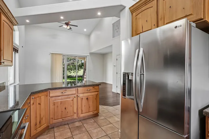 Kitchen featuring stainless steel refrigerator, wood cabinetry, dark countertops, and tile flooring