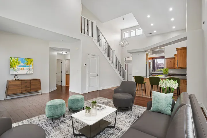 Two-story living area featuring wood-finish flooring, a contemporary staircase with dark balusters, a kitchen pass-through with counter seating, and recessed lighting