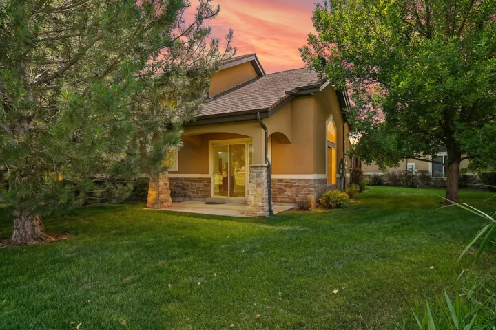 Rear exterior featuring a stucco finish, stone accent siding, pitched shingle roof, and a concrete patio