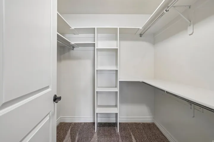 Walk-in closet featuring built-in shelving, multiple hanging rods, and dark-toned carpeting