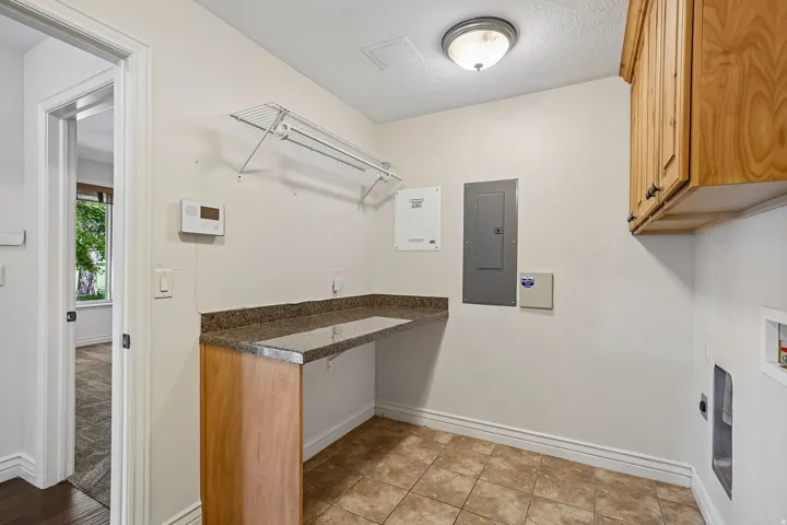 Utility room featuring tile flooring, a built-in countertop with a stone-finish surface, wood-finish cabinetry, a wire shelving system, and an overhead flush-mount light fixture
