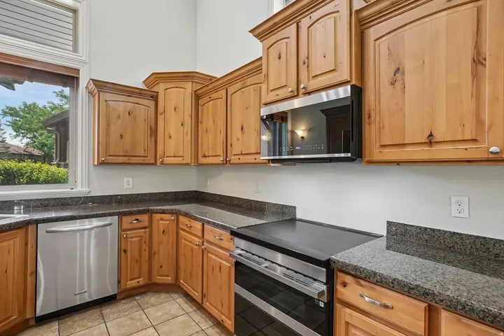 Kitchen featuring light wood cabinetry, dark speckled countertops, stainless steel appliances including a built-in microwave and dishwasher, and tile flooring